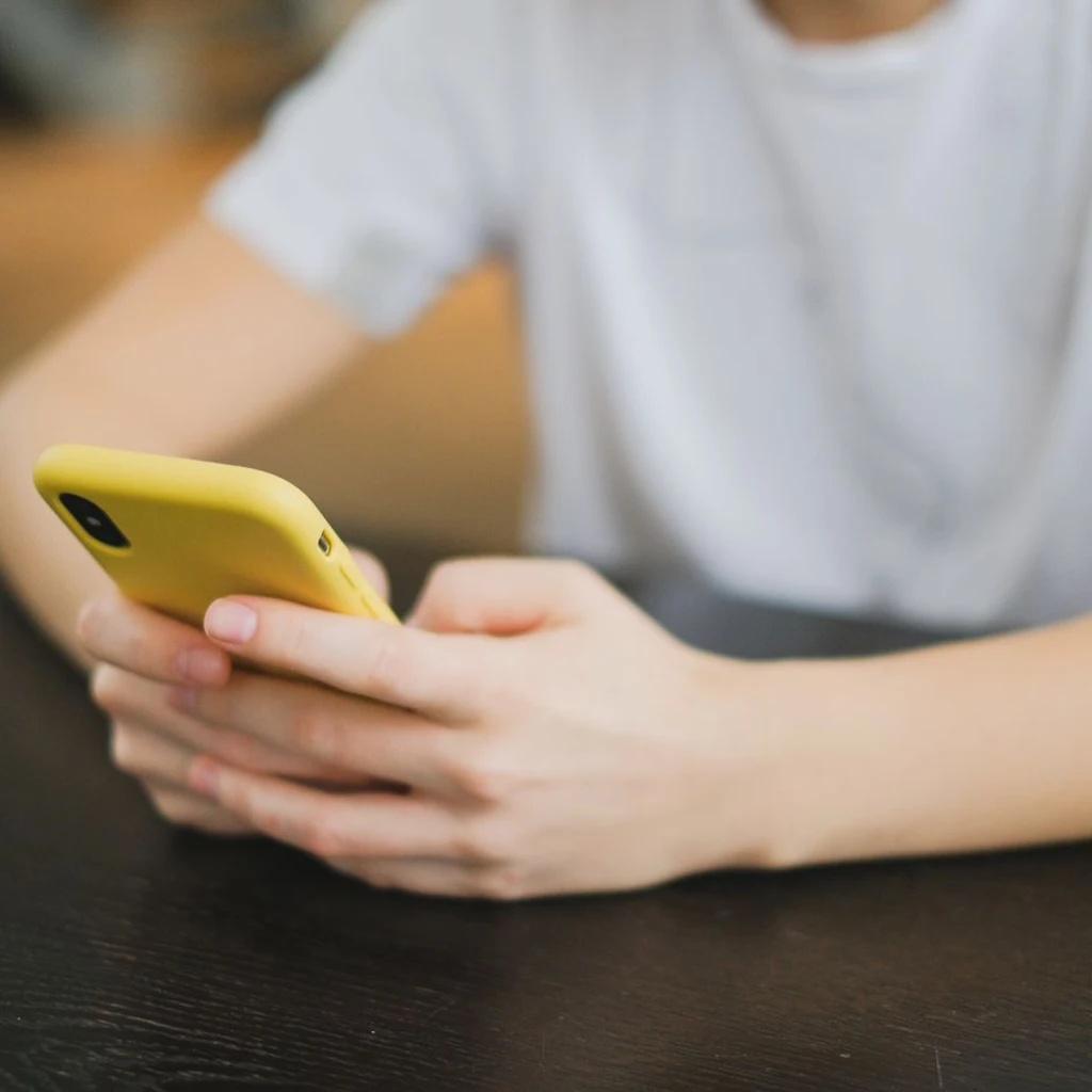 Stockfoto van iemand die thuis een gele smartphone gebruikt